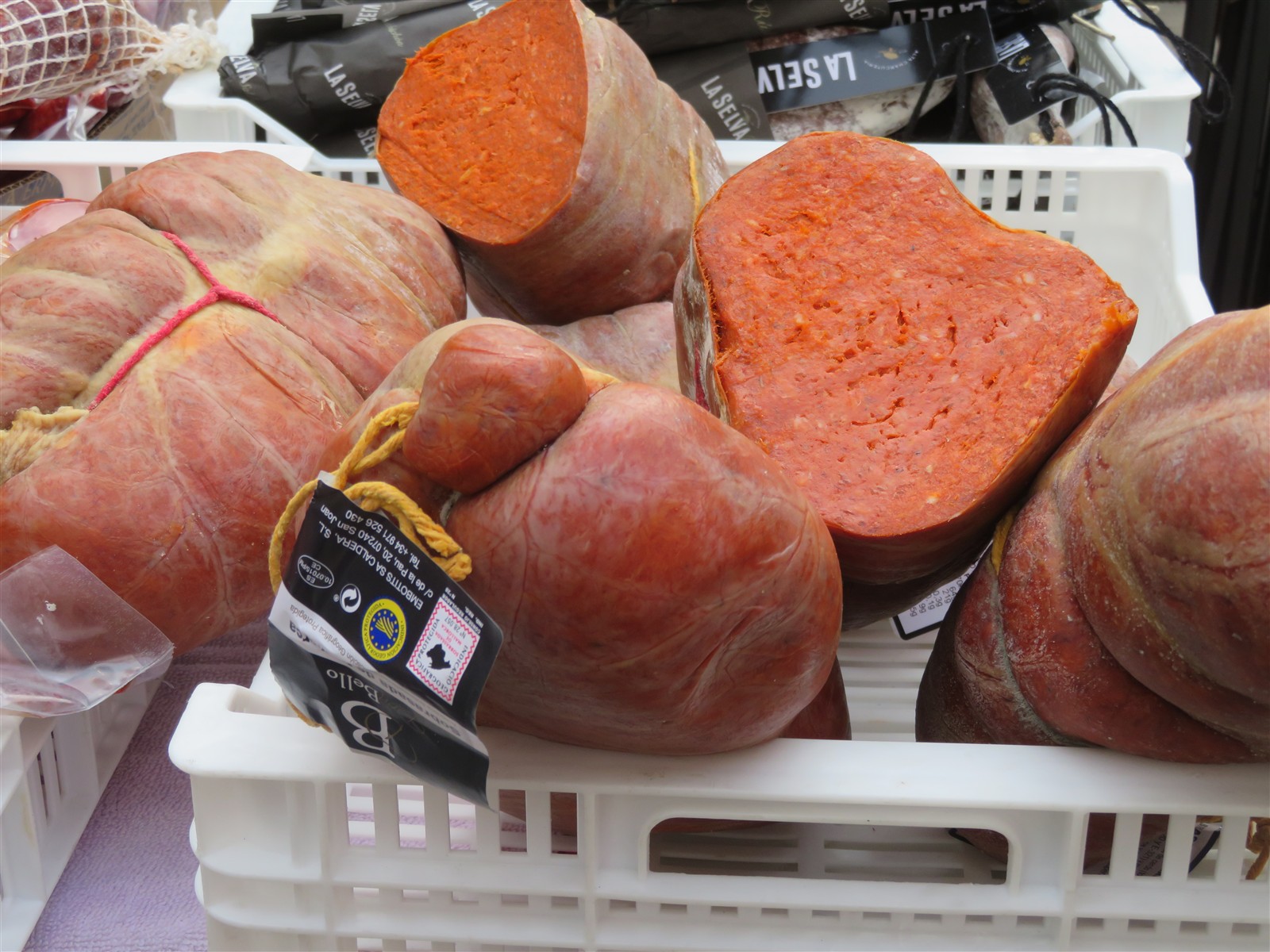 Whole sobrassada de Mallorca sausages in a market crate, one cut open to show the paprika-red paste